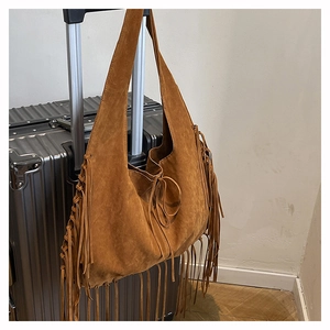 Detail showing brown suede tote bag with long tassels hanging on a suitcase
