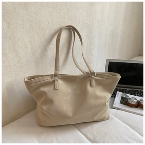 Detail of minimalist cream leather tote bag with slim straps in a cozy office setting