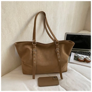 Detail shot of a tan suede tote bag featuring vertical straps and metal ring accents