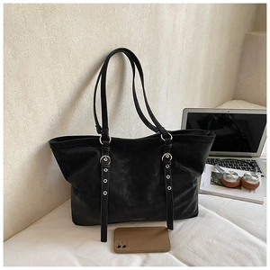 Detail of black suede tote bag with metal eyelets and decorative straps in office setting