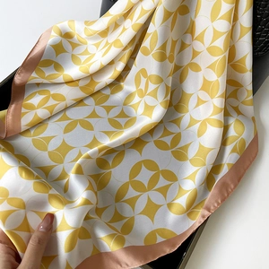 Elegant geometric silk scarf in yellow and white draped over a black leather handbag