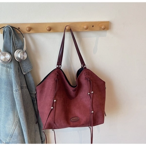 Détail du sac cabas en daim bordeaux avec cordons de serrage et élégantes perles en métal