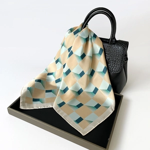 Detail of silk square scarf with green geometric pattern draped on a black leather bag