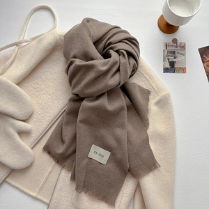 Detail of soft brown knit scarf featuring fine tassel fringe and white brand label