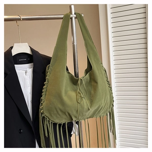 Close-up of green suede tote bag featuring handmade woven edges and long fringe tassels