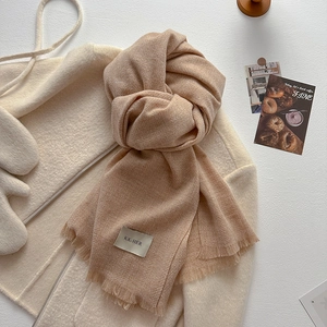 Close-up of light camel knit scarf with fine fringe detail and rectangular woven label