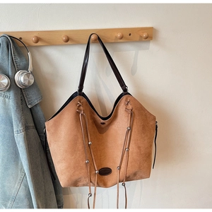 Détail du sac cabas en daim avec cordon à franges, perles en métal et écusson logo