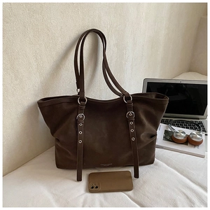 Detailed close-up of dark brown suede tote bag with metallic buckles in an office setting