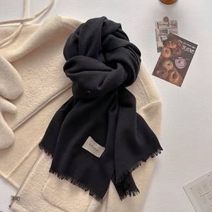 Detail of a thick black scarf with fringe and minimalist label on a beige coat background