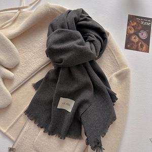 Close-up of charcoal grey winter scarf texture with fringe on beige wool coat