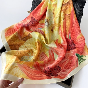 Detail of satin square scarf with sunflower print draped over a black handbag