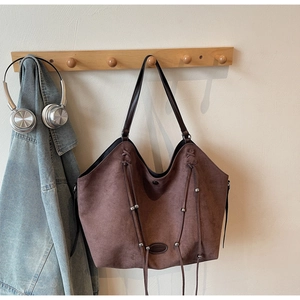 Détail d'un sac cabas en daim marron avec des pompons à franges et perles en métal