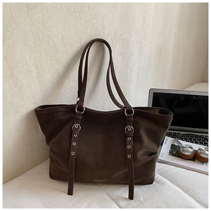 Close-up of matte dark brown leather tote bag detail with decorative metal buckle straps