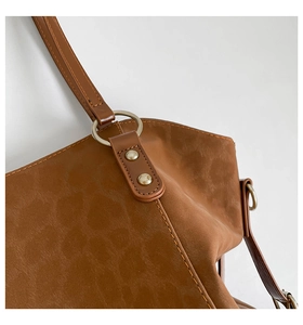 Close-up of brown suede tote bag featuring gold metal rings and reinforced rivets