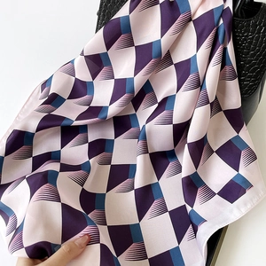 Elegant silk scarf with purple geometric cube patterns draped on a black leather handbag