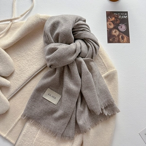 Close-up of light gray knitted scarf texture with fringe details and a small brand label