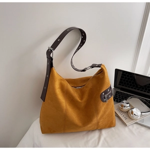 Detail view of mustard yellow suede tote bag featuring brown strap and silver eyelets