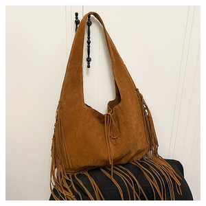 Detail of bohemian tan suede tote bag with long vintage fringe hanging on a white hook