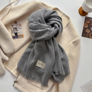 Detailed view of grey fringe scarf with brand label on soft sherpa jacket background
