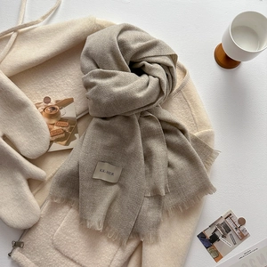Detail view of oatmeal knit scarf with tassels and KK-HER brand tag on soft fabric