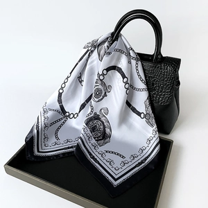 Detail view of a chain print silk scarf draped over a black crocodile pattern handbag