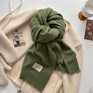 Detail of green scarf with tassel fringes and brand label on white tabletop