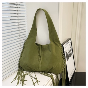 Detail of green suede tote bag featuring long bohemian tassels and woven side laces