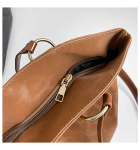 Detailed close-up of smooth brown leather tote bag with zip closure and metallic rings
