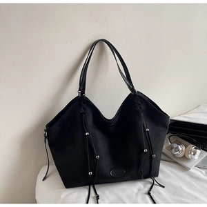 Détail d'un sac cabas noir en daim avec tressage latéral, franges et perles métalliques