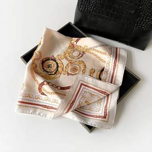 Detailed view of silk square scarf with golden chain patterns on a black display tray