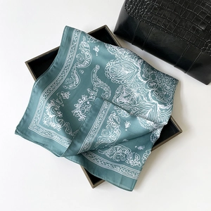 Carré en soie vert avec motifs paisley blancs raffinés sur un plateau noir élégant