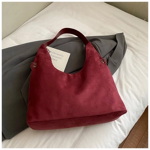 Detail der burgunderroten Hobo-Tasche mit Nieten und matter Wildleder-Optik auf weißem Bett