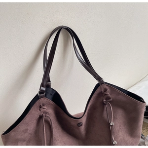 Détail du sac cabas en daim marron avec cordon de serrage tressé et perles métalliques