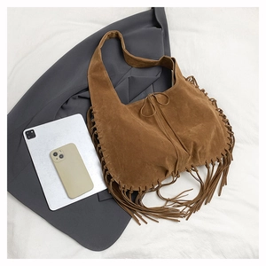 Close-up of brown suede hobo bag with woven edges and long fringes on stylish background