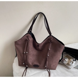 Détail d'un cabas en daim marron foncé avec glands en cuir et perles métalliques