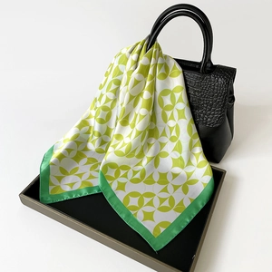 Green and white geometric silk scarf draped elegantly over a black leather handbag handle