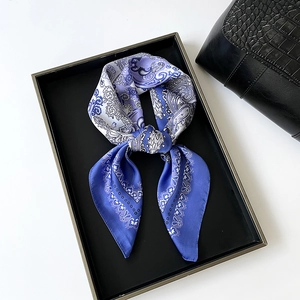 Detail of elegant paisley silk scarf tied in a bow on a black tray with handbag