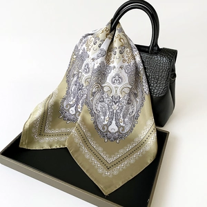 Detailed view of silk neckerchief with golden paisley pattern tied on a black handbag