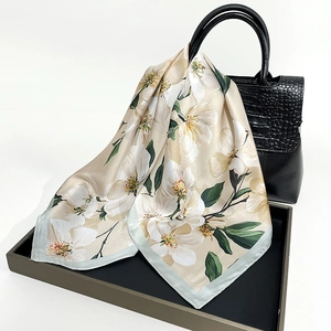Elegant satin scarf with white magnolia flowers draped over a black handbag