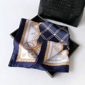 Détail d'un foulard carré en soie avec motifs de chaînes dorées sur un sac à main