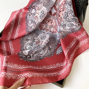 Elegant paisley silk scarf in burgundy and black draped on a classic handbag