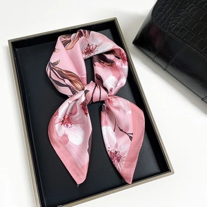 Close-up of pink satin square scarf with magnolia floral print on a black luxury handbag
