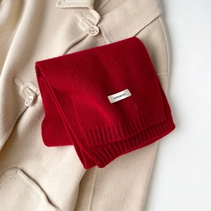 Dettaglio della sciarpa in maglia di 100% lana rossa con bordo a coste ed etichetta