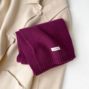 Dettaglio di una sciarpa in maglia 100% lana viola scuro su un cappotto in lana beige