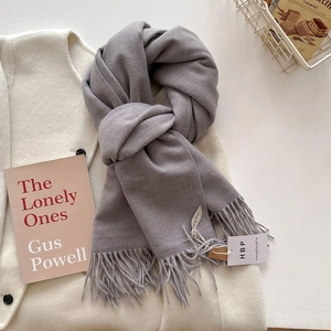 Détail de l'écharpe gris clair aspect cachemire avec franges sur un manteau blanc