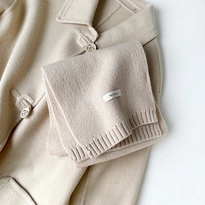Dettaglio sciarpa in 100% lana beige con trama a costine e bottone con logo in rilievo