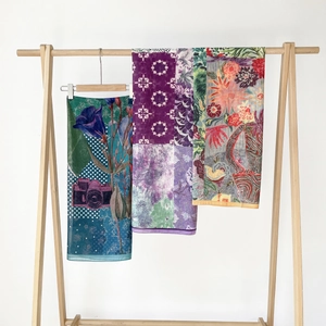 Tre foulard di seta stampati su grucce di legno con motivi floreali e geometrici