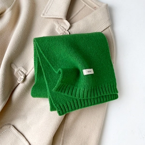 Dettaglio dell'etichetta 100% lana su sciarpa in maglia verde con bordi a coste sottili