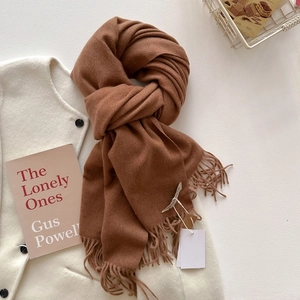 Détail d'une écharpe marron foncé à franges sur un gilet en laine blanche à boutons