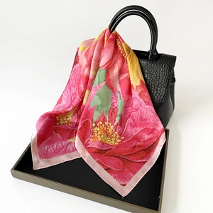 Pink and red sunflower silk scarf with floral print draped over a black handbag